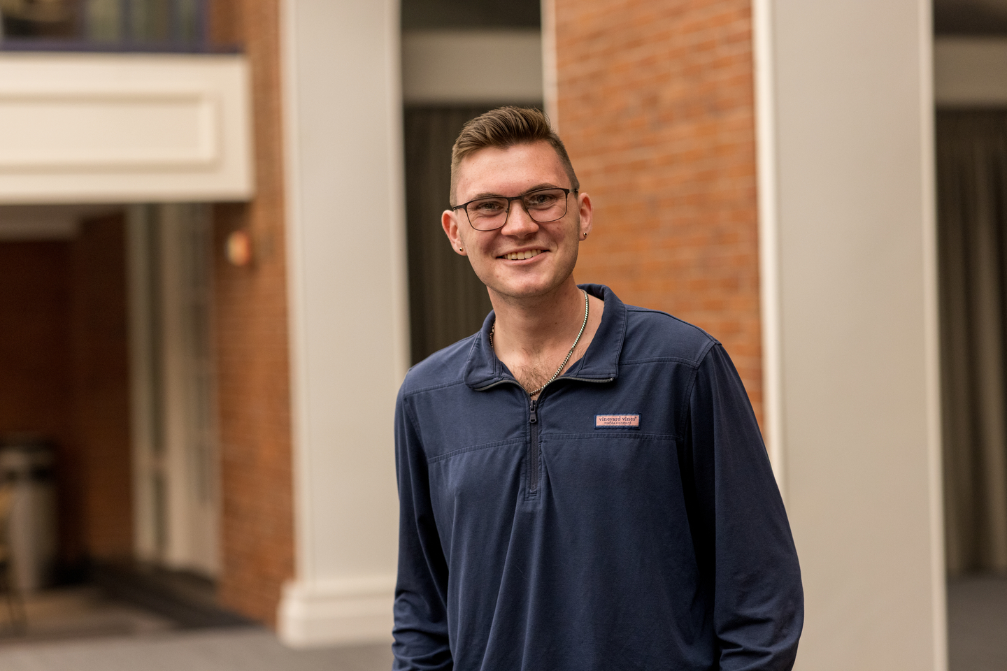 Andrew Fox wearing a blue shirt and eye glass and standing in front of brick and white columns