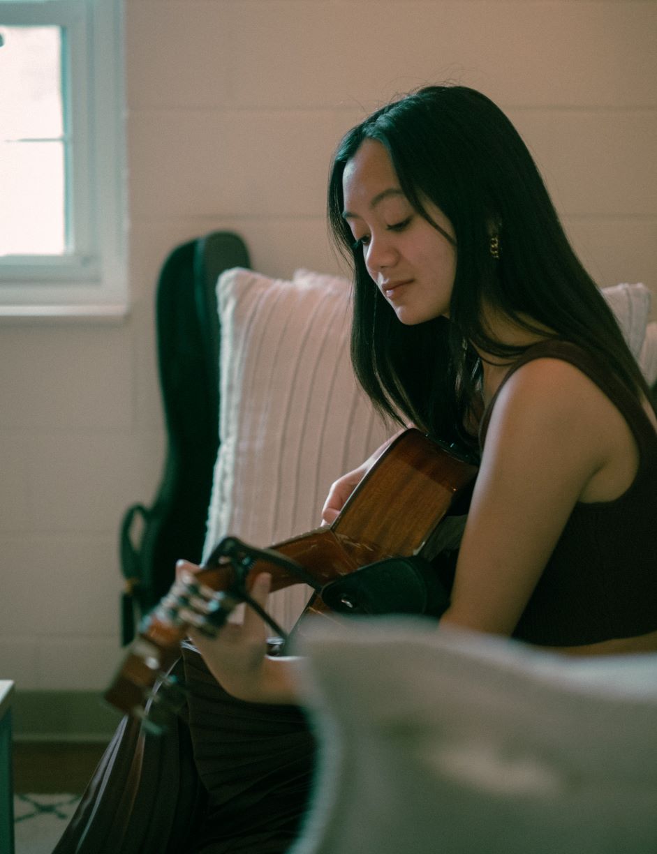 Bethany Barber sitting on a couch playing guitar