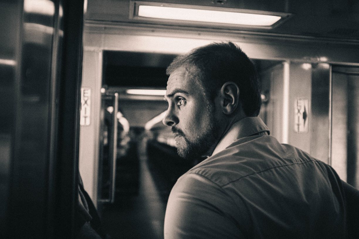 Avery Heinz stands inside an MBTA commuter rail car, looking off into the distance.