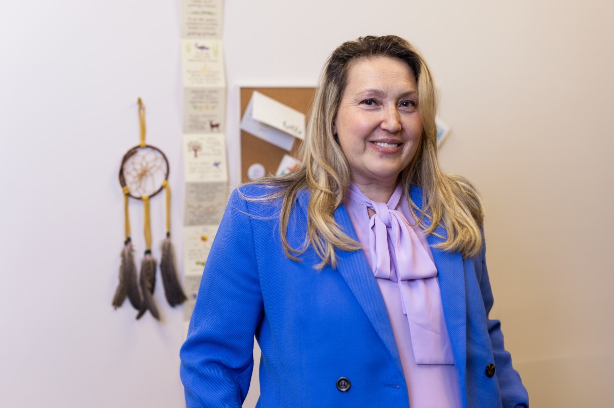 Georgia Madway poses in front of a corkboard in her office, wearing a lavender blouse and cornflower blue blazer.