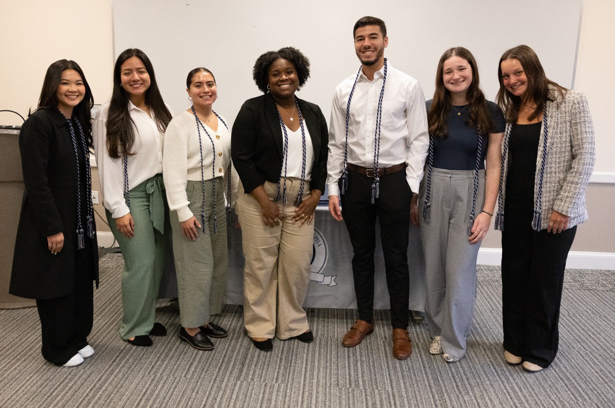 Seven students — all members of Tri-Alpha and Bentley's Class of 2024 — pose with the braided and tasseled cords representing their membership in the honor society that they will wear during graduation.