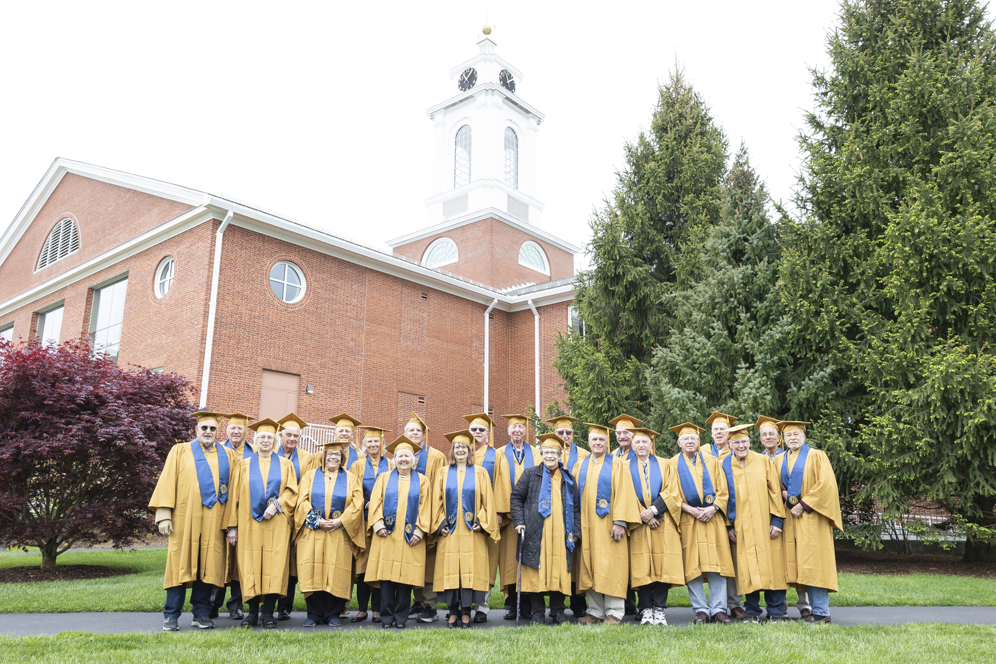 Bentley alumni celebrating 50+ Reunions pose for a photo in regalia with the Bentley Library in the background