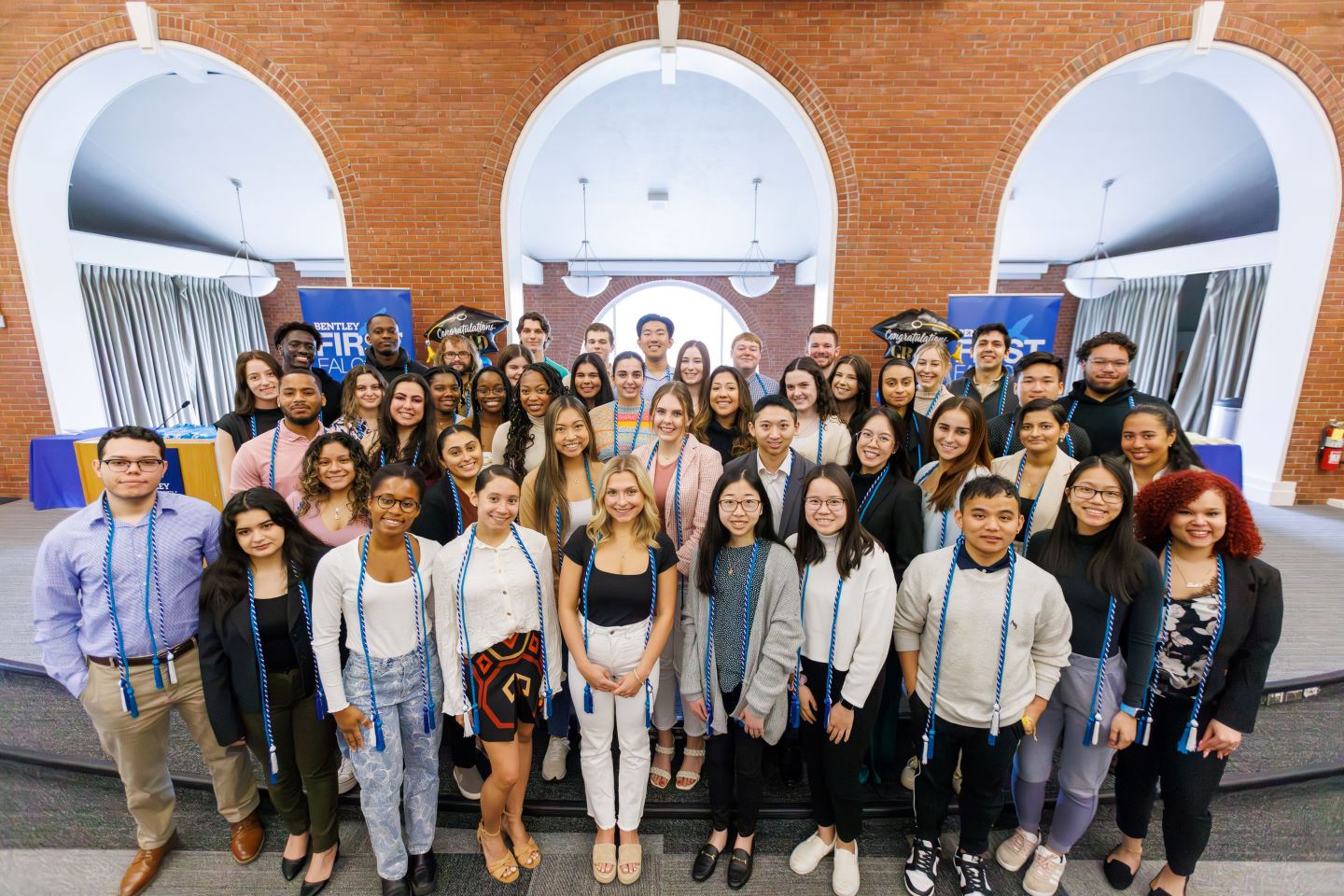 Group of first-gen graduating Bentley seniors gathered on stage at a cording ceremony