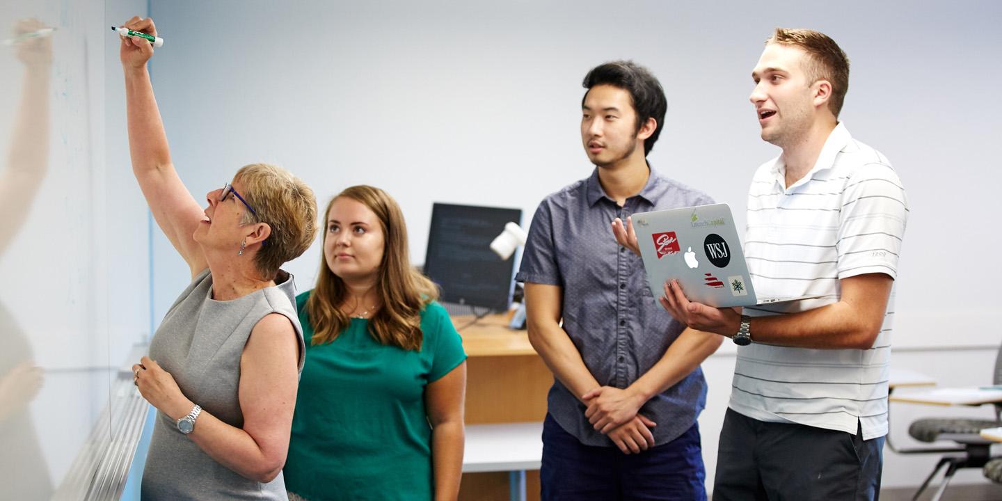 three students work with teacher at whiteboard