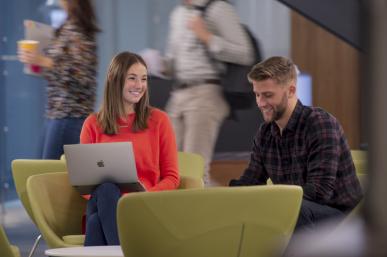 Two students sitting and conversing with students walking in background