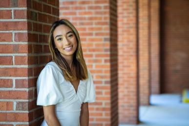 Kimiya Kim '22 wearing white blouse and standing outside in front of a brick building on campus