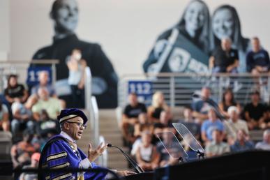 Bentley President E. LaBrent Chrite standing at podium wearing regalia addressing a crowd