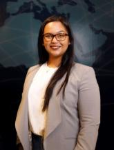 Kerisse Seepersad standing in front of wall map wearing white shirt and tan blazer