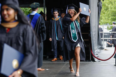 A student holds up her diploma triumphantly as she crosses the stage 